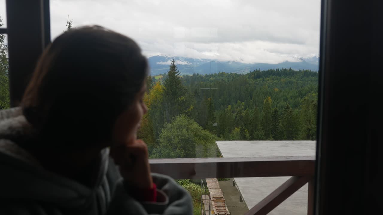 mujer mirando una vista de la montaña desde una ventana