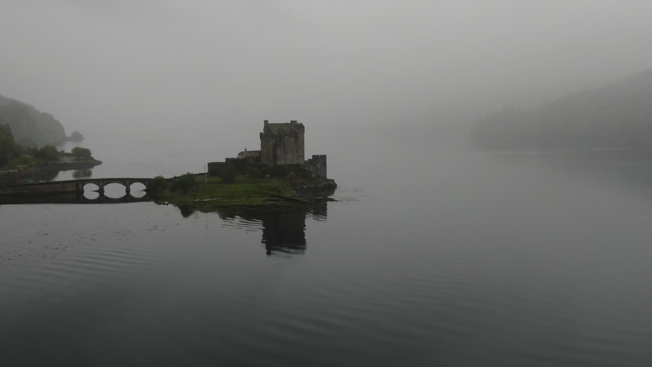 Eilean Donan Castle, a famous Scottish castle, is shrouded in fog, creating a mysterious and evocative atmosphere