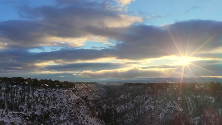 Ampia vista aerea della città e dei quartieri residenziali spolverati di neve sul bordo del canyon. L'alba spettacolare e le nuvole risaltano il freddo paesaggio invernale boschivo del sud-ovest