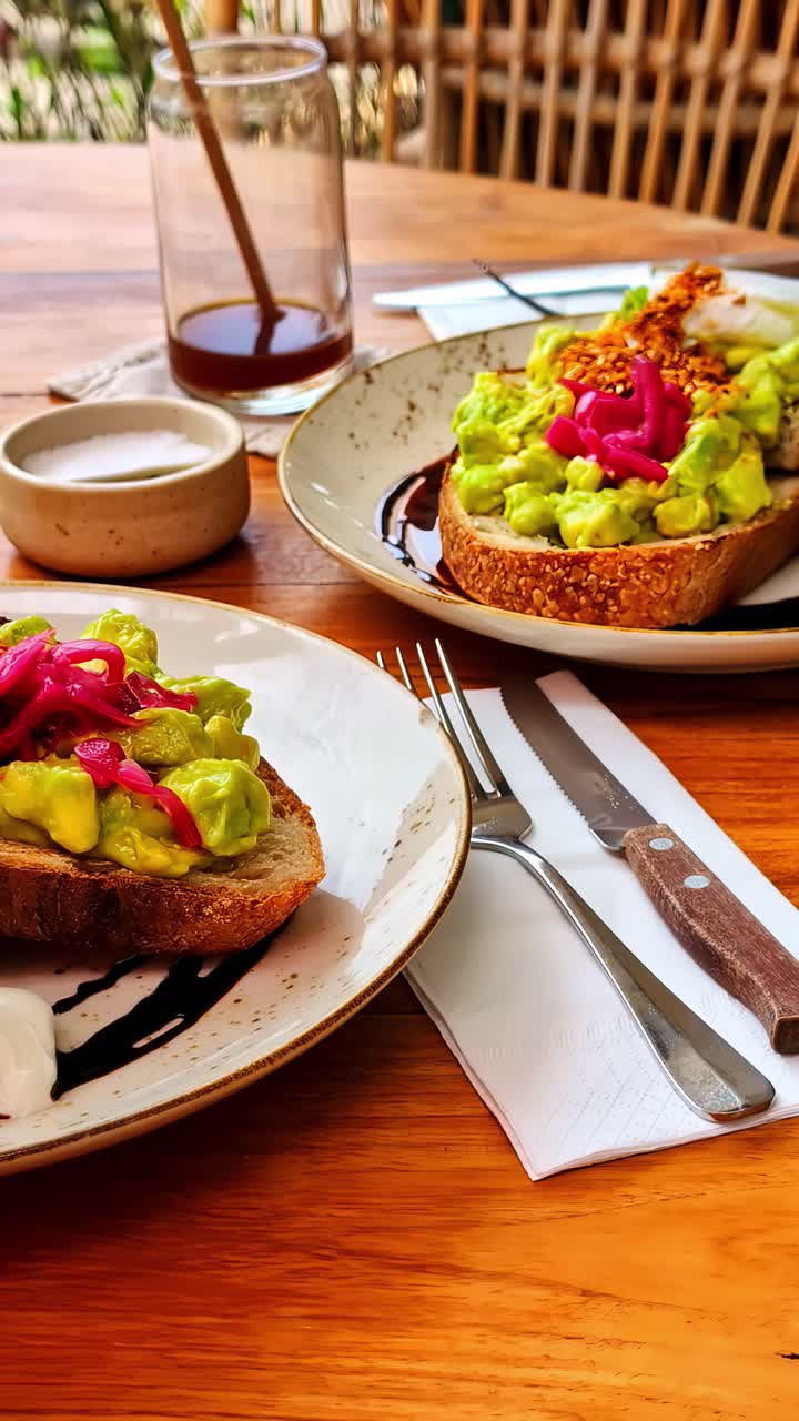 Toast con avocado schiacciato e cipolle sott'aceto su un tavolo di legno di un caffè, sotto una luce solare intensa.