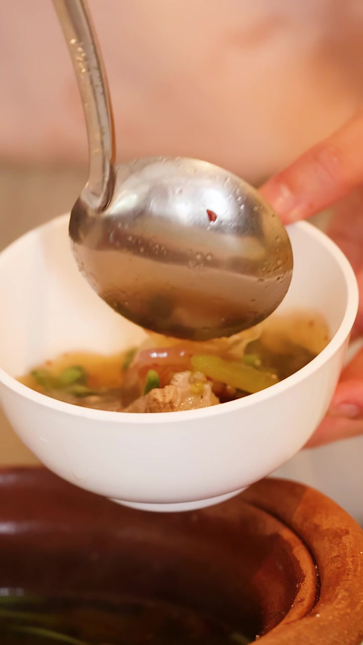 Mestolo che versa zuppa thailandese piccante da una pentola di terracotta tradizionale in una ciotola bianca.