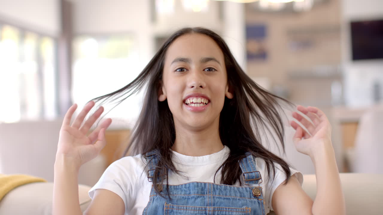 Smiling teenage girl in denim overalls sitting on couch at home