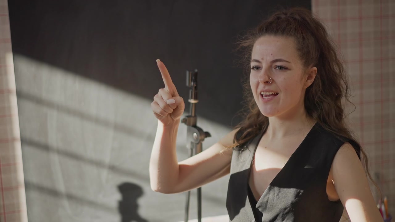 Giovane donna bianca in una sessione di coaching per audizioni, pratica intensa in studio con il coach in primo piano, esercizi di controllo del respiro e proiezione vocale vicino al microfono, interpretazione emotiva e critica del mentore per la musica.