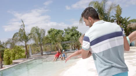 Portrait-of-happy-caucasian-father-and-son-playing-at-swimming-pool-at-beach-house