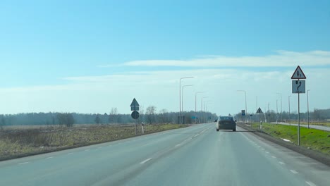 front view of driving on the asphalt motorway. ahead is vehicles moving on highway against blue sky, streetlights along the road. grassy field by the road and pedestrian path. pov forward driving view
