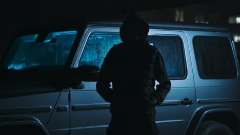 hombre oscuro frente a un auto en la noche