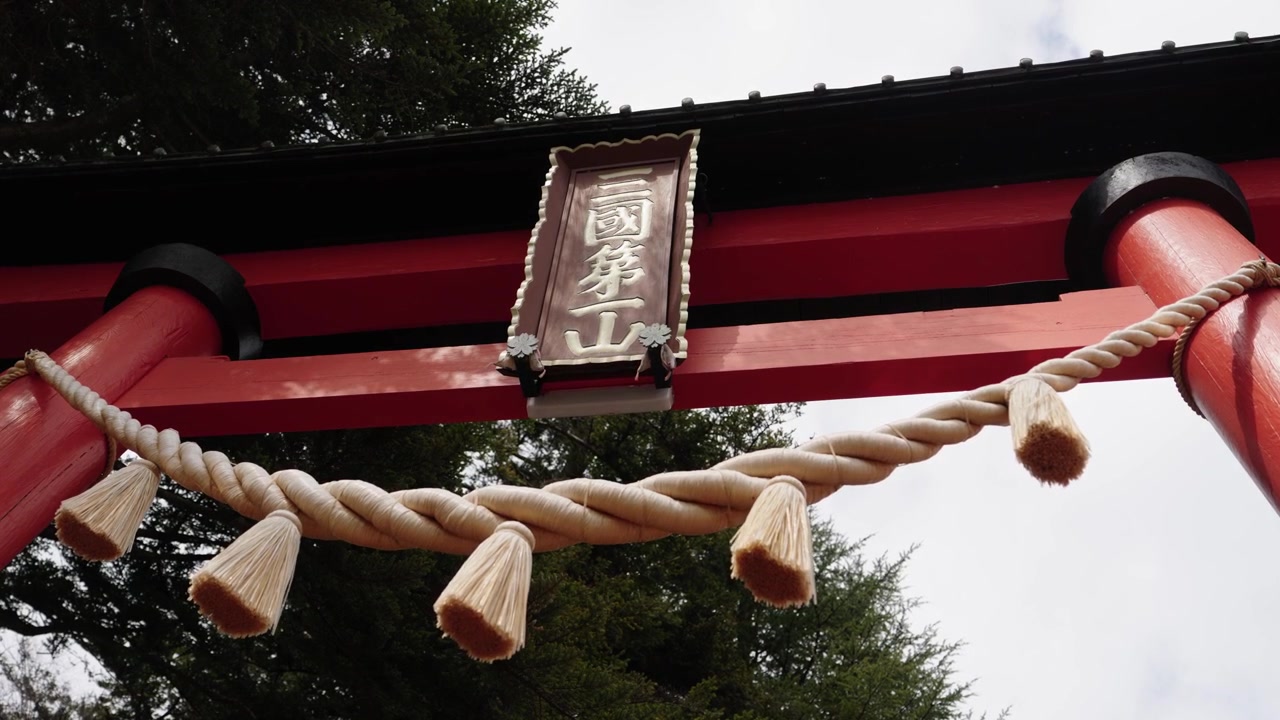 Closeup of red torii gate with shimenawa rope tassels and kanji inscription plaque
