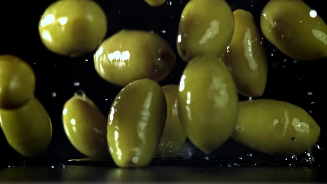 Olive verdi che cadono e schizzano su una superficie scura al rallentatore