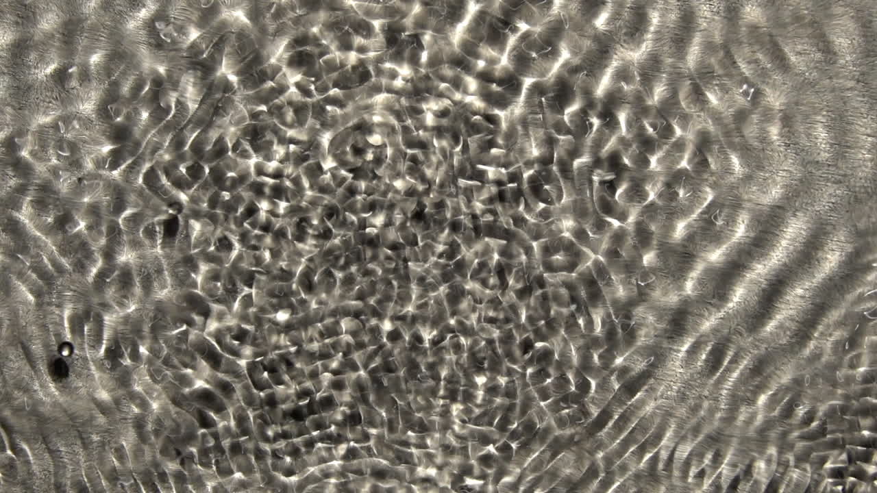 los patrones de ondas vibratorias que cambian rápidamente se superponen, con una gota esférica suspendida en la superficie del líquido