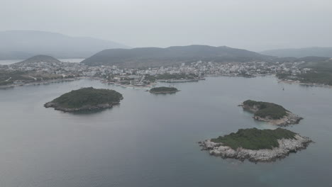 drone shot flying over the water over the small islands in front of ksamil albania in the morning on a cloudy grey day with boats around and haze in the sky log