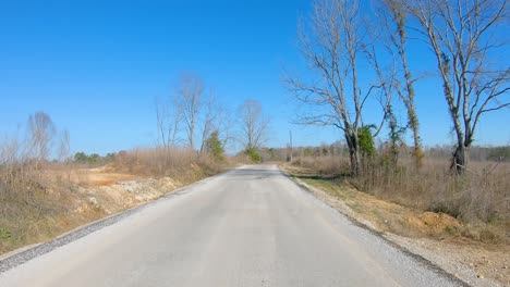 POV-driving-a-rural-county-road-past-dry-grassland-and-thru-a-wooded-area-in-northern-Mississippi-USA-on-a-sunny-winter-day