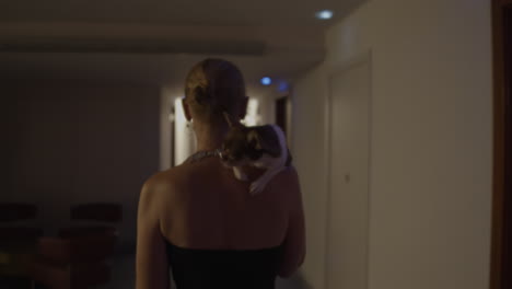 mujer llevando un chihuahua en un corredor del hotel por la noche