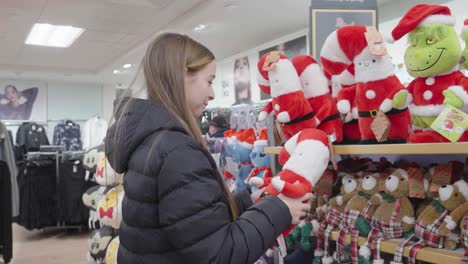 christmas is coming as young female looks at santa dolls in shop display