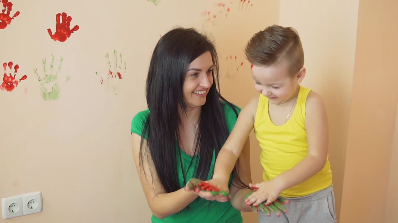 madre joven con su pequeño hijo están mezclando colores en sus manos usted deja hermosas huellas de manos en la pared. madre e hijo