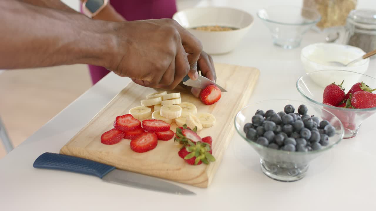 Mani che raccolgono una fragola intera e affettano rondelle sottili su un tagliere per la colazione.