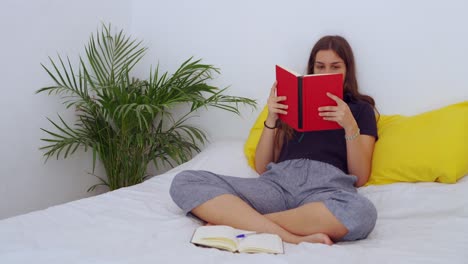 Mujer-Joven-Sentada-En-La-Cama-Y-Leyendo-Un-Libro.