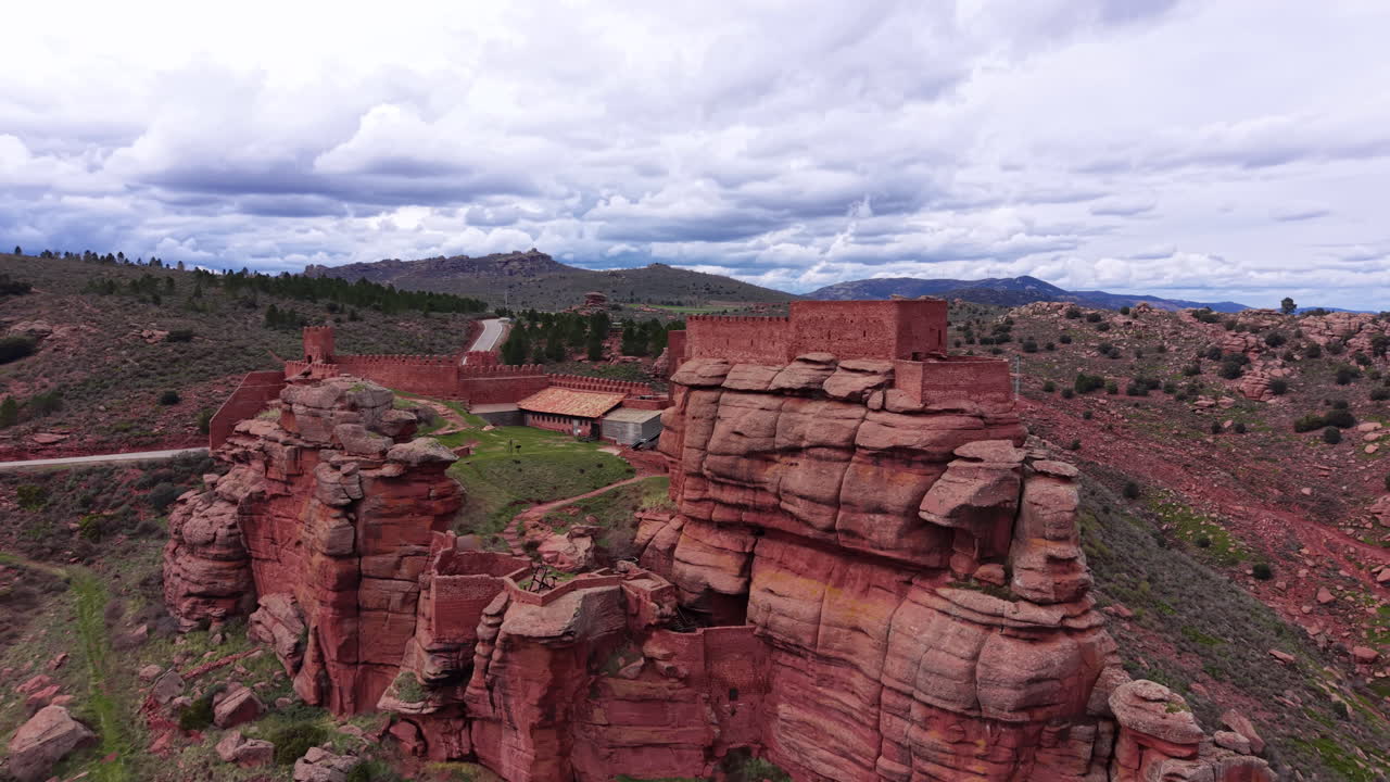 Vista aerea del Castello di Peracense costruito tra scogliere di arenaria rossa, caratterizzato da mura fortificate, torri e terreno accidentato in Aragona, che evidenzia l'architettura difensiva medievale.
