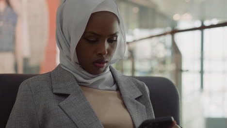 black woman in hijab surfs internet on smartphone in office