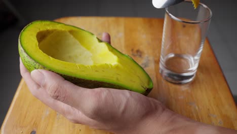 Scooping-out-ripe-avocado-with-a-spoon,-placing-it-in-a-glass