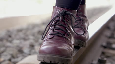 close up of young woman with purple boots and black leggins keeping her balance walking along the train tracks