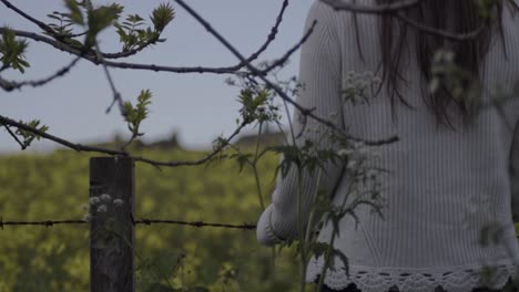 Carefree-woman-looks-at-view-through-field-of-rapeseed-in-countryside-landscape