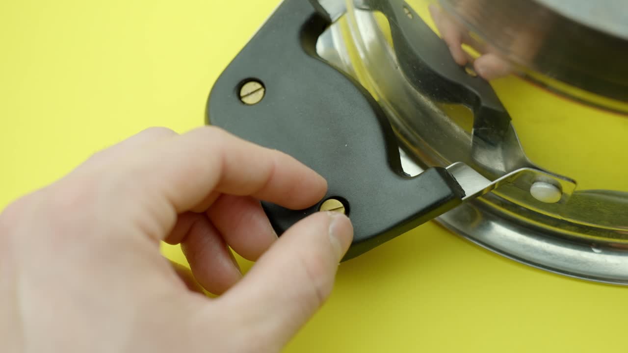 Detailed view of a person repairing boiler, using screwdriver to secure screws on black boiler cover, with yellow background, highlighting precision work, home appliance maintenance, and DIY skills.