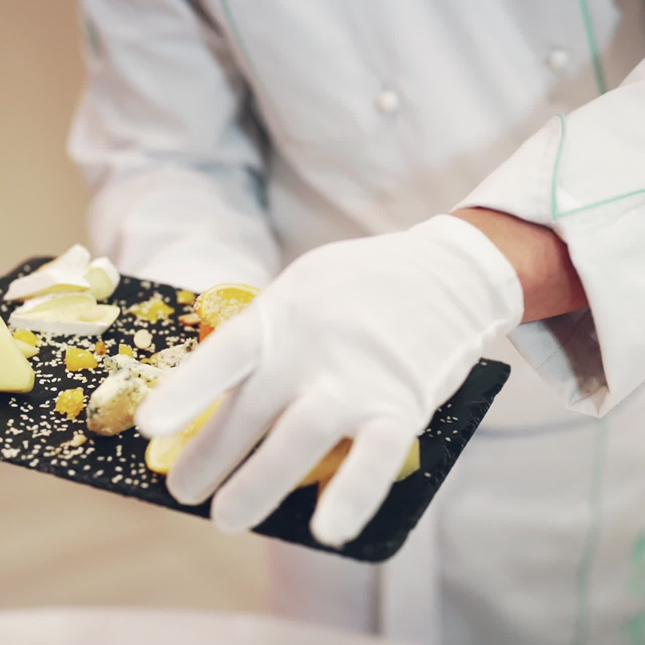 Delicious appetizer of different kinds of cheese decorated by a piece of fresh lemon with a chef in white gloves. Beautiful presentation of cheese on the black surface in the restaurant.