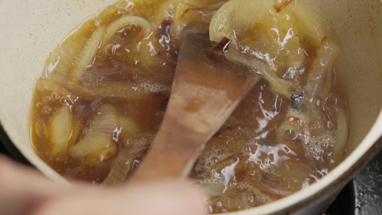 Slow motion close up of a fresh potato slice falling into a boiling vegetable stew. This nutritious meal is being cooked in a modern kitchen in a residential home