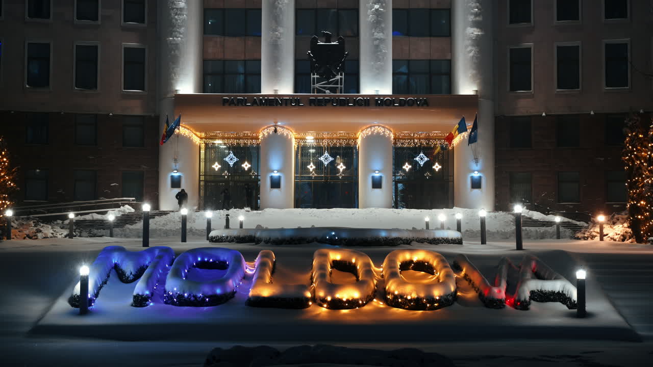 Parliament of the Republic of Moldova with national emblem, illumination and Christmas decorations in the evening. Ground covered in snow. Winter in Chisinau