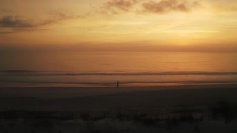 aerial, silhouette of person running on the beach by coastline during golden hour