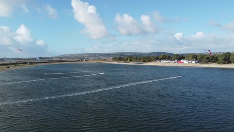 Aerial-Tracking-Shot-Of-Kite-Surfers-Racing-Across-Fiesta-Island-Park-In-Mission-Bay,-San-Diego