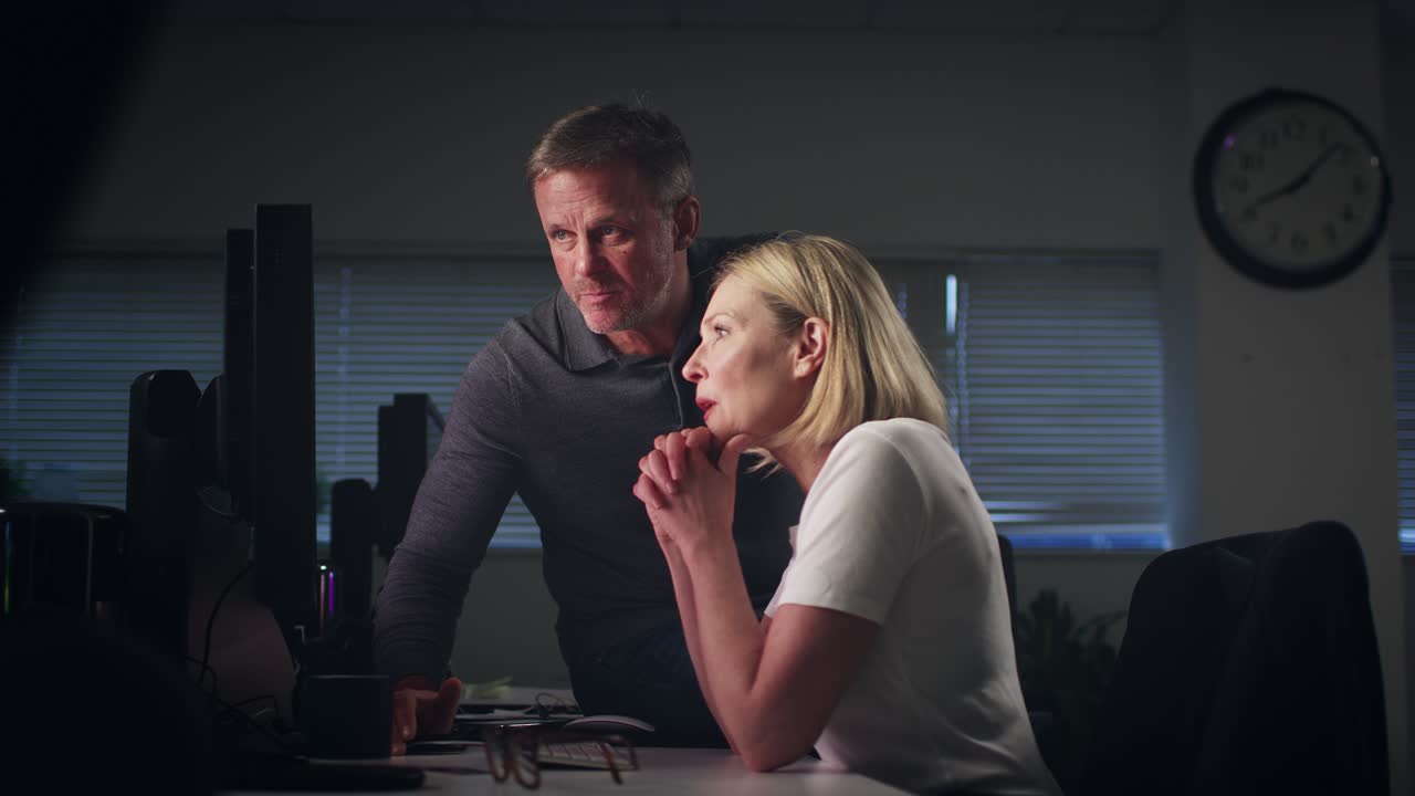 Mature businessman and  businesswoman having informal meeting sitting at desk in office working late - shot in slow motion
