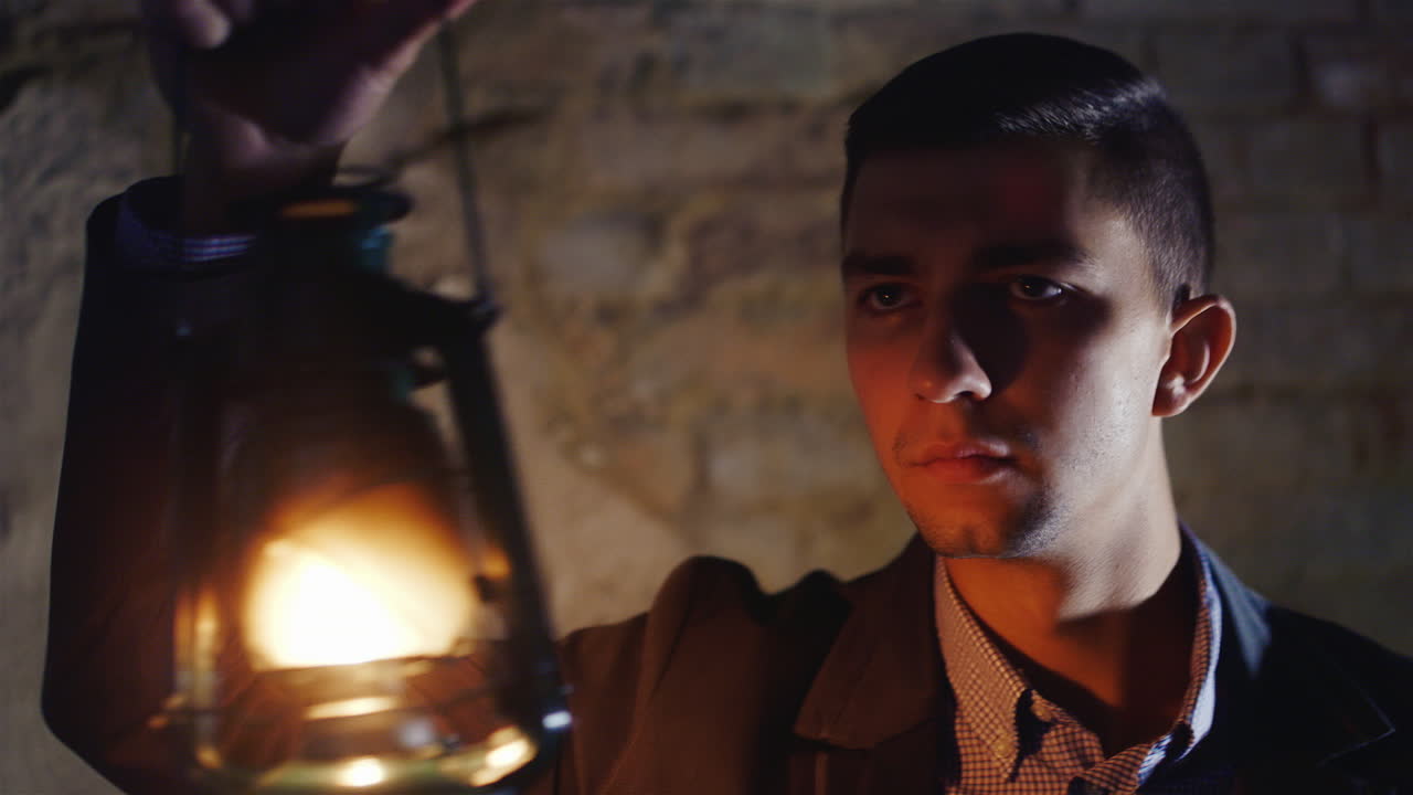 испуганный молодой человек в темном коридоре, держащий в руке масляную лампу, одетый в костюм