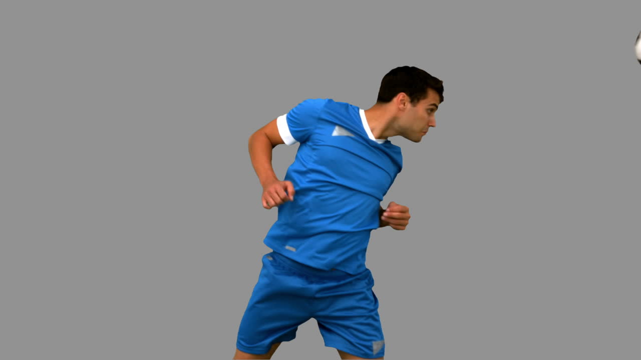 Attractive man heading a football on grey screen