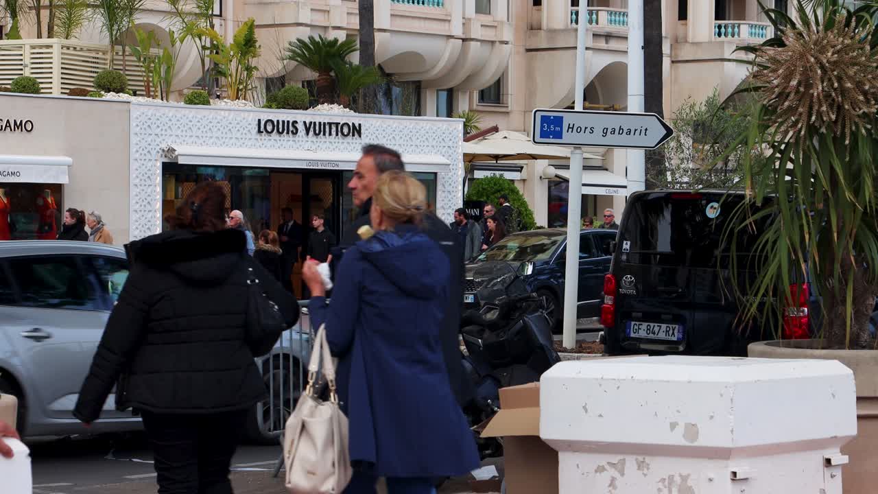 Luxury shoppers and cars outside Louis Vuitton store in Cannes, France, on busy street
