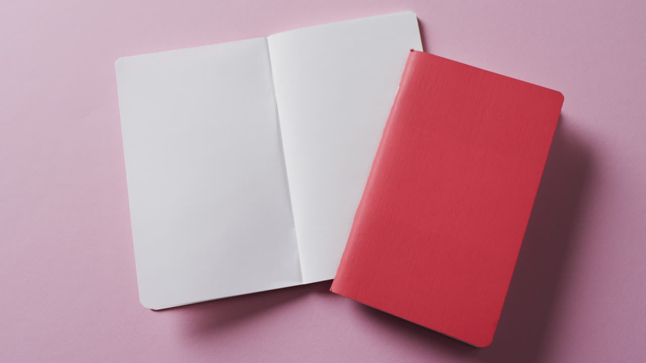 Close up of open blank book and red closed book with copy space on pink background in slow motion