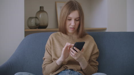 business woman typing message on mobile phone at home office. young girl chatting on phone in slow motion. close up young woman hands using smartphone on couch.