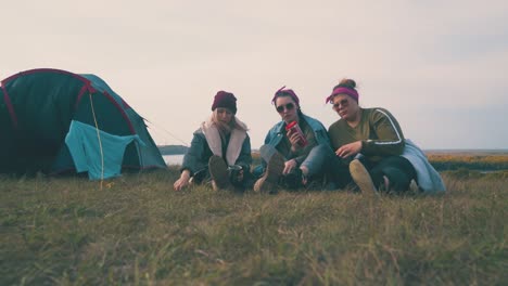 girl-tourists-with-drinks-sit-on-grass-by-tent-at-sunset