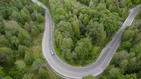 Tracking-Drone-shot-of-a-SUV-car-making-a-turn-on-a-road-surrounded-by-lush-green-forests-in-Ontario