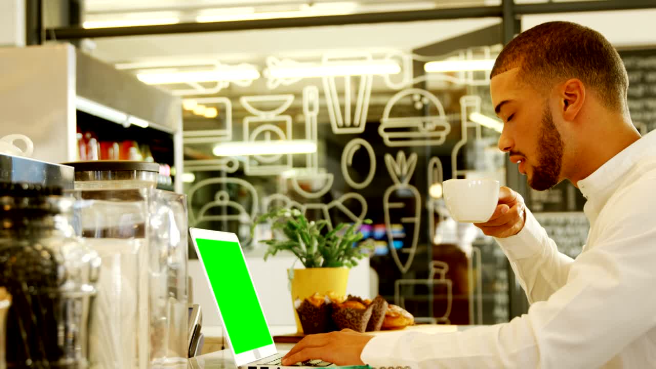 Uomo attraente che usa il laptop mentre prende il caffè 4k