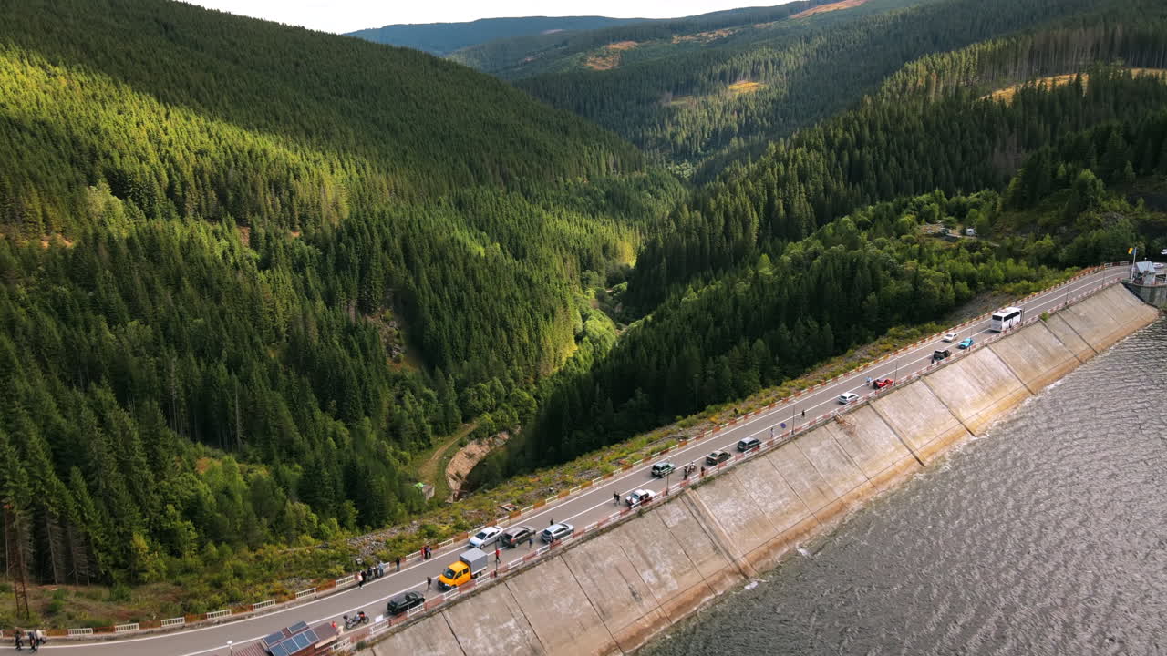 Aerial drone view of the Oasa Dam in Romania. Carpathian mountains, hills with lush forest, multiple visitors and cars