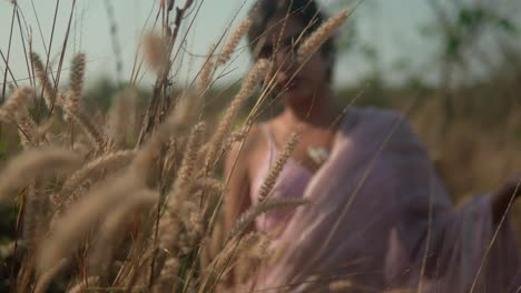 Mujer-Vestida-De-Rosa-Disfrutando-De-Un-Momento-Sereno-En-El-Campo-De-Trigo-Dorado-Al-Atardecer,-Enfoque-Suave