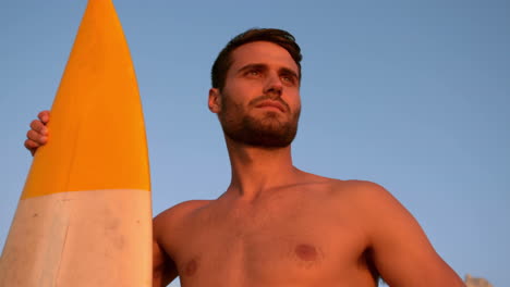 hombre sin camisa con una tabla de surf mirando hacia la playa