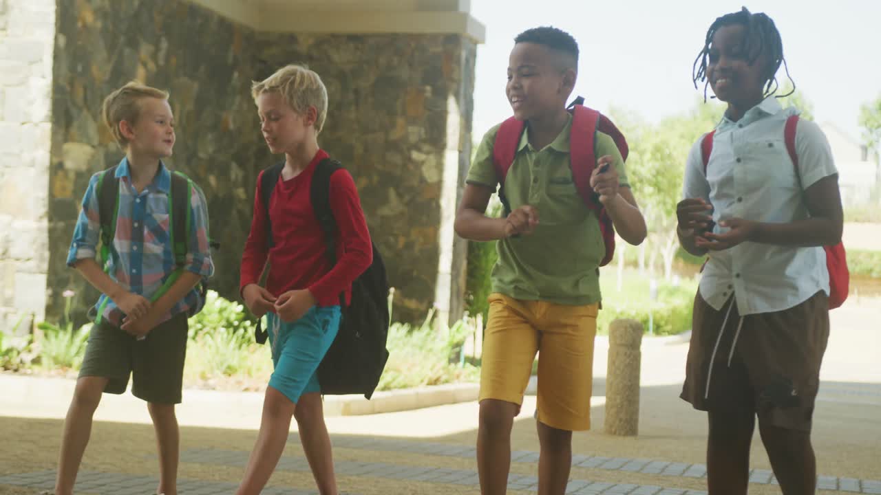 Video of happy diverse boys walking and talking in front of school