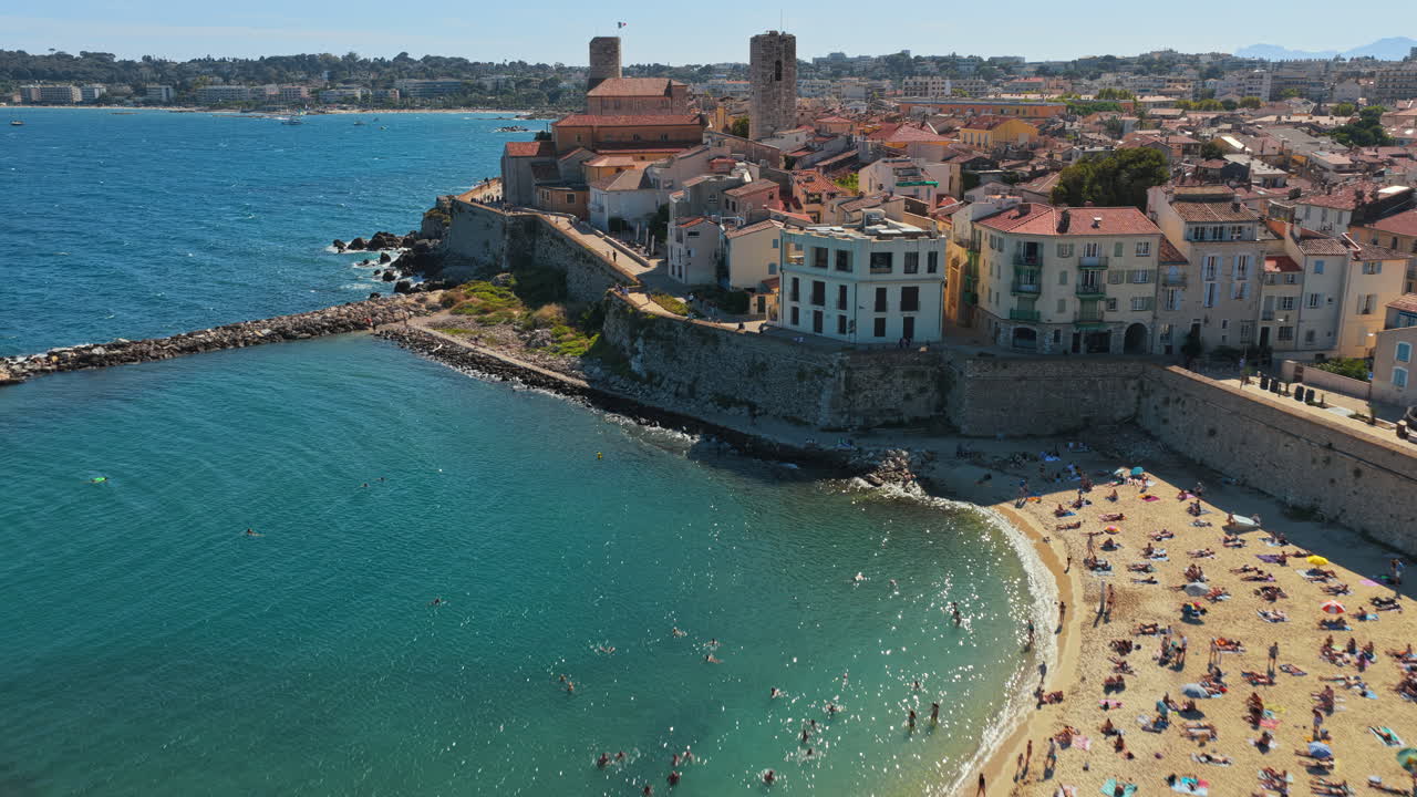 Aerial drone view of Antibes Old Town, medieval ramparts, sandy beach, and marina with yachts, seen from above the sea