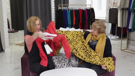 two elderly women are sitting on a sofa in the middle of the store and looking at clothes