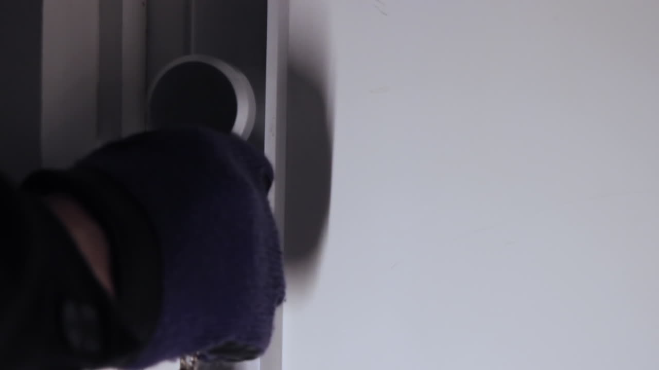 primer plano de una figura oscura que abre una puerta con un juego de llaves y guantes