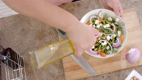 hands of biracial woman dressing salad with olive oil in kitchen, copy space, slow motion