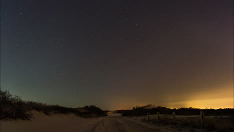 Un-Hermoso-Cielo-Nocturno-Estrellado-Gira-Sobre-Un-Camino-De-Tierra-En-La-Playa-Rodeada-De-Dunas