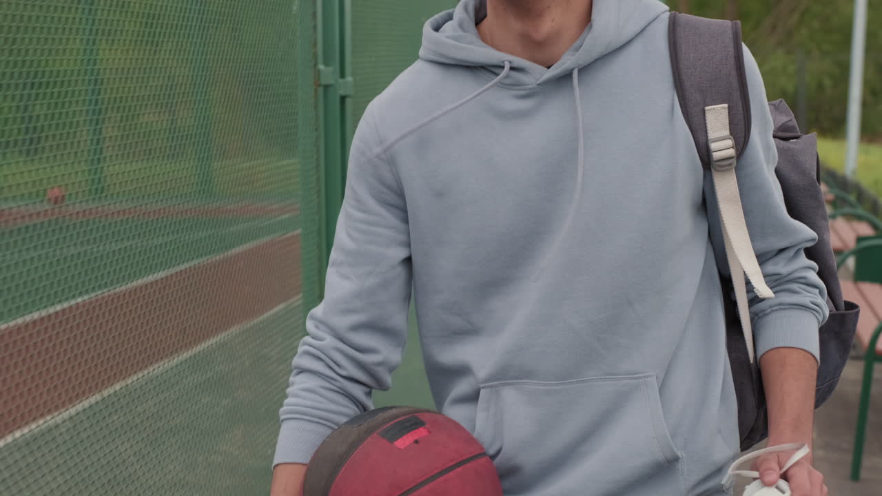 Young Man with Ball Walking beside Outdoor Basketball Court